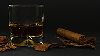 Ein gefülltes Whiskey-Glas und ein Zigarillo liegen auf einer dunklen Tischoberfläche nebeneinander.