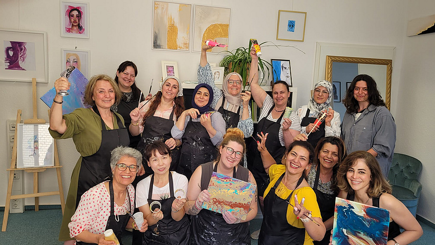 Eine Gruppe Frauen verschiedener Nationalitäten auf einem Gruppenfoto mit Kunstwerkzeugen