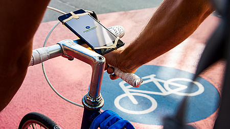 Fahrrad auf einem Fahrradweg mit einem am Lenker befestigten Smartphone, auf dem die STADTRADELN-App geöffnet ist