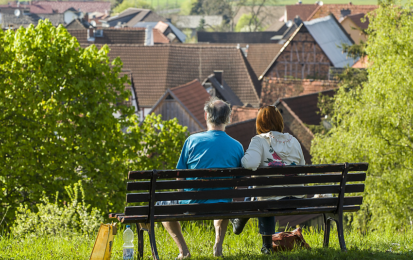 Ein Mann und eine Frau sitzen auf einer Bank. Sie sind von hinten zu sehen.