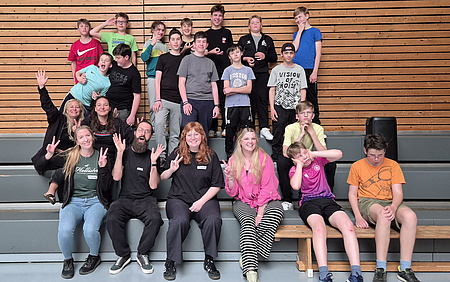 Junge Menschen die in einer Halle auf einer Treppe sitzen und in die Kamera schauen