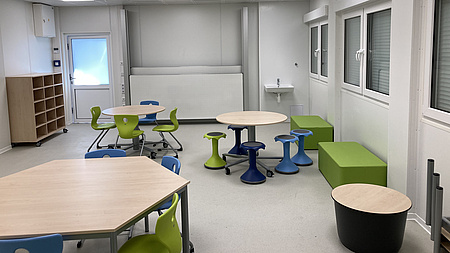 2 kleine runde Tische mit Hockern, 1 eckiger Tisch mit Stühlen, ein offenes Regal