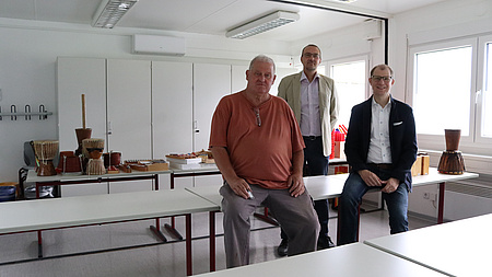 Drei Männer sitzen in einem Klassenzimmer auf einem Tisch.